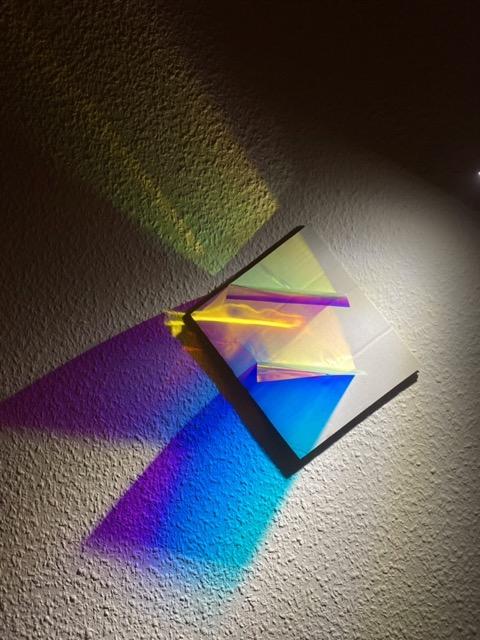 Iridescent foil in a straight shape is illuminated from above with a spotlight, creating colored light reflections.