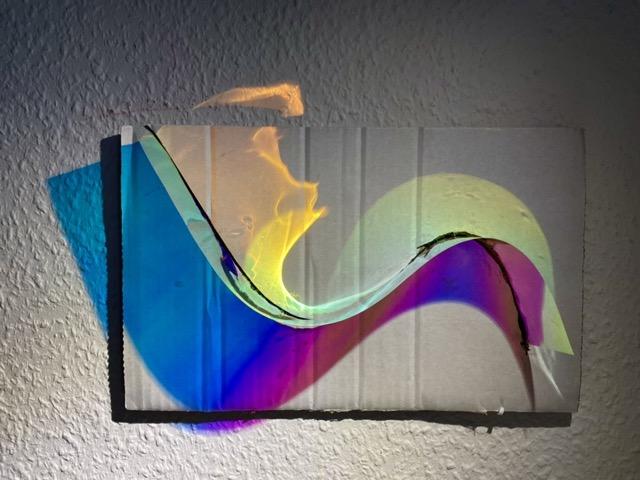 Iridescent foil in a curved shape is illuminated from above with a spotlight, creating colored light reflections.