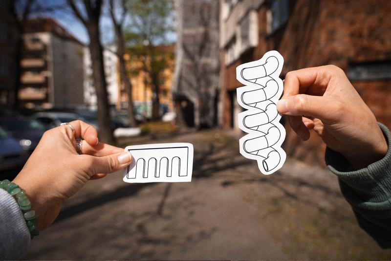Hände halten gezeichnete Spielplatzelemente vor einem Straßenhintergrund