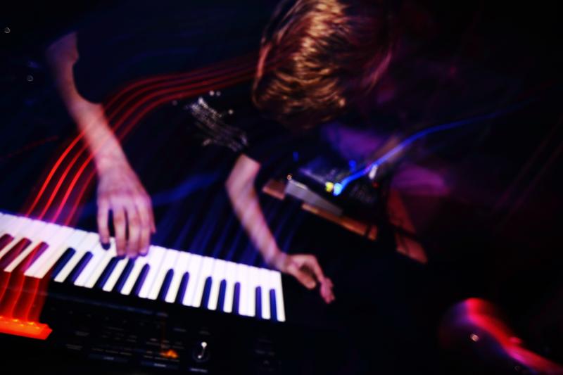 bm_128 spielt in einem dunklen Raum auf einem Keyboard.