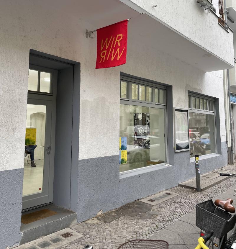 The red WIRWIR flag with yellow text hangs above the door of the project space.