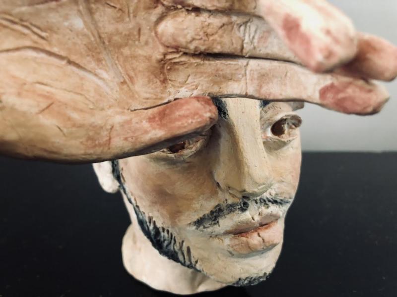 Image of a face made of clay partially hidden by a hand also made of clay