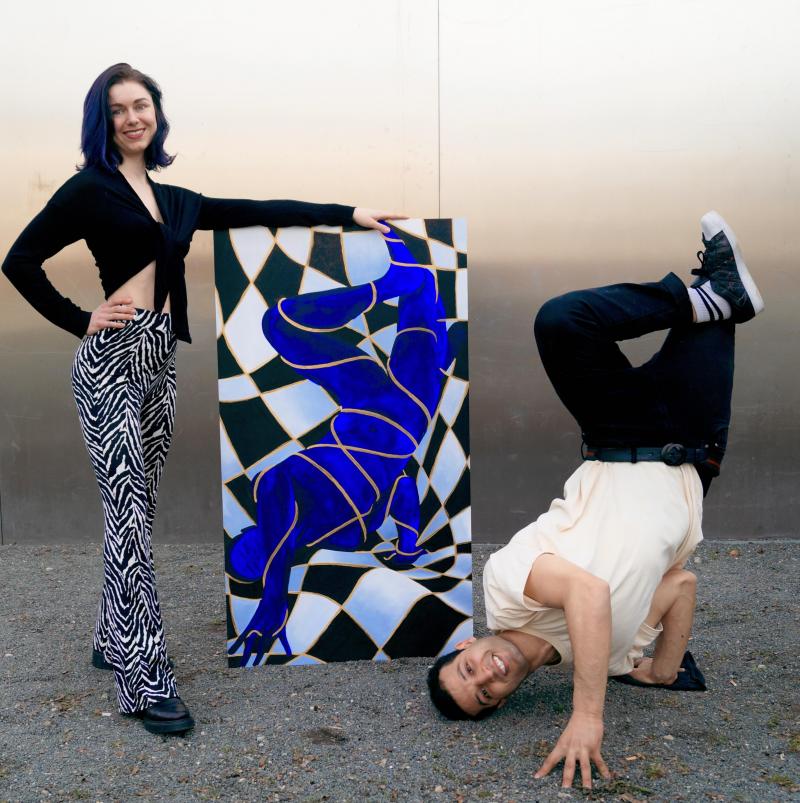 Vor einem grauen Hintergrund steht links eine junge Frau in Zebra-Leggings. In der Mitte steht ein Gemälde, welches einen blauen männlichen Körper in einer Breakdance-Pose zeigt. Rechts neben dem Gemälde ist ein junger Mann in schwarzer Jeans, Sneakers und weißem T-Shirt in ebendieser Pose zu sehen. 