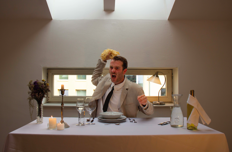 Fotografie eines elegant gekleideten Mannes, der entgeistert Spaghetti durch den Raum wirft