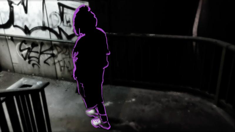 Eine junge Frau geht durch eine graffiti-bemalte Unterführung. Sie trägt eine dicke Jacke mit Kapuze und ist von uns abgewandt. Das Foto ist schwarzweiss und ihre Umrisse sind mit leuchtendem lila Strich nachgezogen und hervorgehoben. 