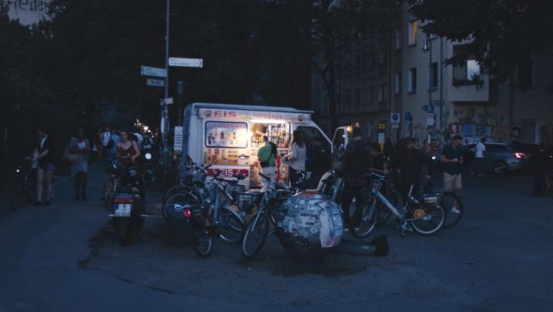 Ein Eisverkaufswagen am Abend. Menschen kaufen Eis und schieben ihr Fahrrad Richtung Tempelhofer Feld.