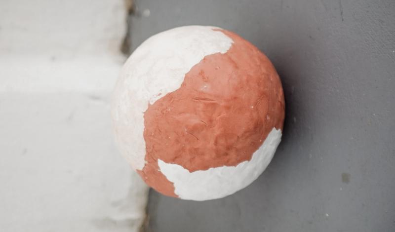 A ball with 2 different kind of clays lays on the floor. Ein Ball mit 2 verschiedenen Arten von Ton liegt auf dem Boden.