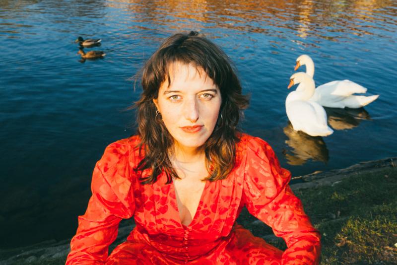 Porträt einer Frau in rotem Kleid vor einem Teich mit Schwänen
