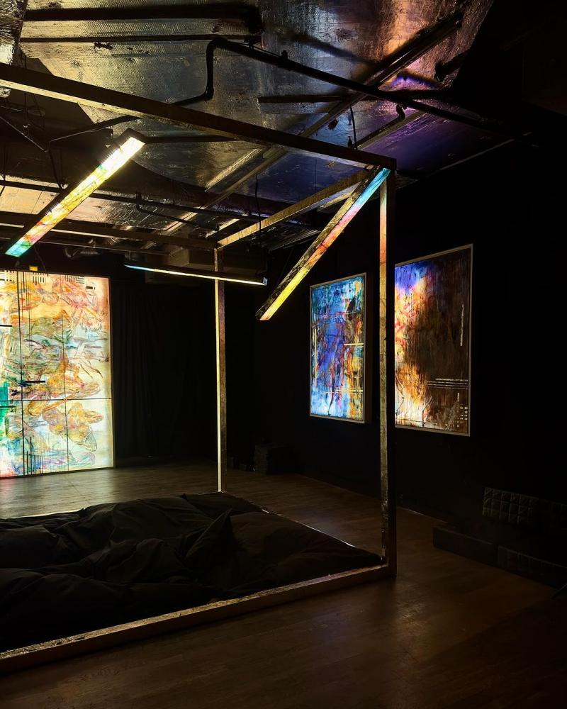 An installation consisting of a metal structure surrounded by backlit paintings in the middle of an otherwise dark room