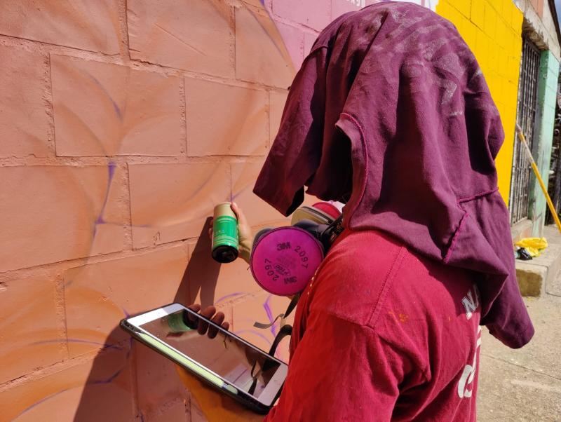 Food of War resident artist "Simio" in the process of painting the Edible Mural