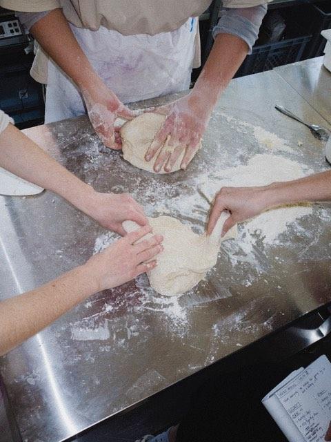 Several Hands of fermentors busy touching and shaping sourdough. 