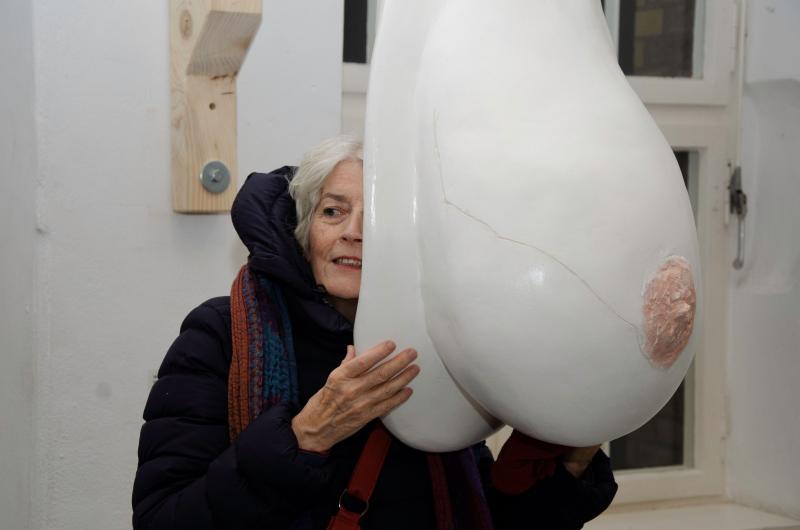 Frau umfasst eine Skulptur in Form einer Brust und horcht in sie hinein
