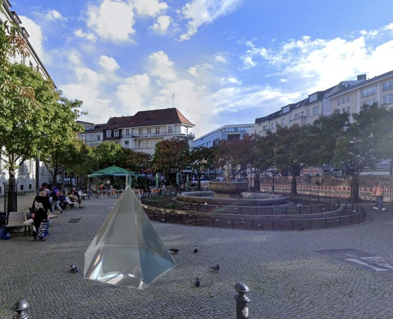 Eine diamantförmige Skulptur aus halbtransparenter Silberfolie steht auf einem öffentlichen Platz in Berlin.