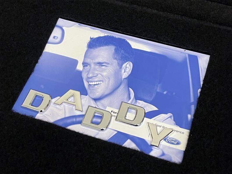 Das Deckblatt einer Betriebsanleitung eines Autos, auf dem ein Mann beim Autofahren abgebildet ist, eingebettet in eine Tuning-Automatte. Auf dem Deckblatt steht mit Chrombuchstaben "Daddy".