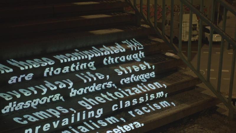 Gwisin Tour image_1: A nighttime projection of fragmented white text on an outdoor staircase, resembling ghostly traces.