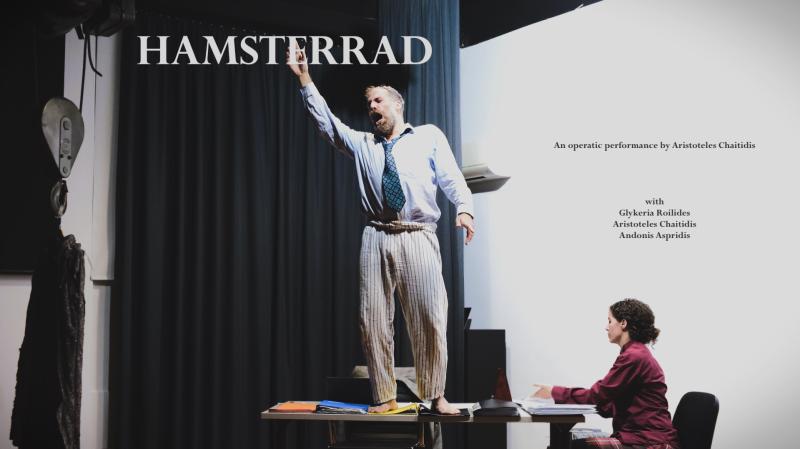 In der Bildmitte steht ein Mann auf einem Tisch mit erhobener Hand und weit geöffnetem Mund. Rechts von ihm sitzt eine Frau am Tisch und arbeitet. Oben der Schriftzug: Hamsterrad. Rechts vor weißem Hintergrund der Schriftzug: An operatic performance und die Namen der teilnehmenden Künstler.