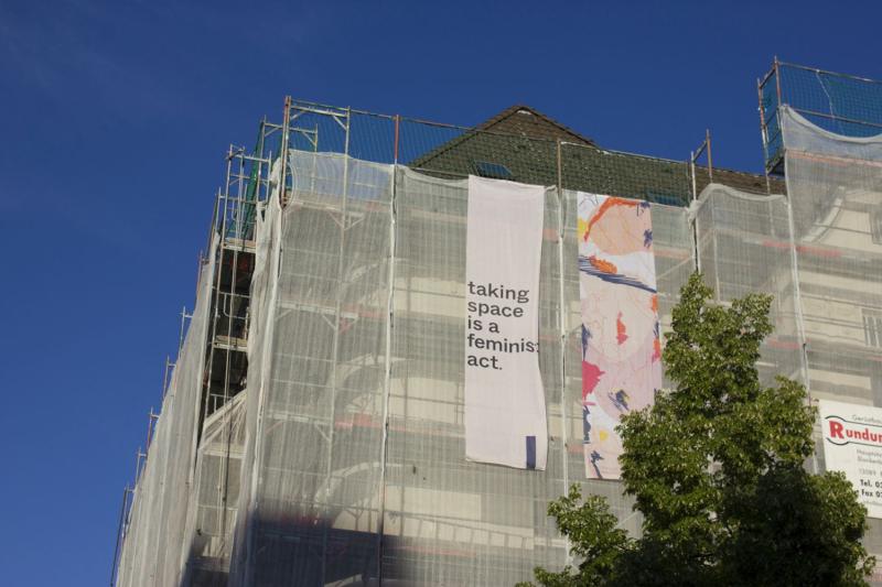 Auf einem Baugerüst hängt ein Banner mit dem Schriftzug "Taking space is a feminist act"