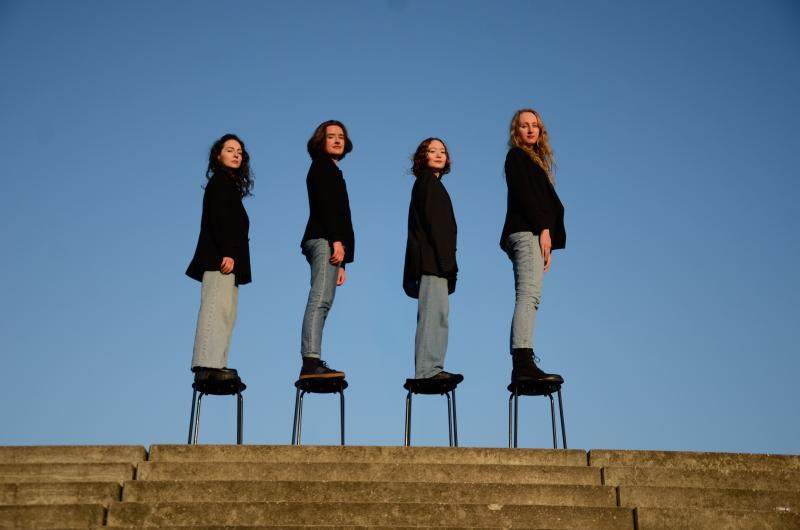 4 Frauen stehen hintereinander auf Hockern vor blauem Himmel