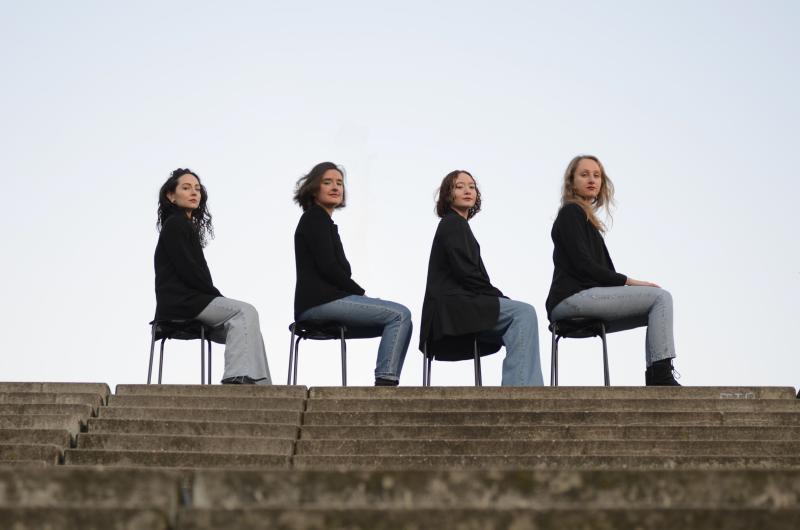 Vier Frauen sitzen auf Hockern und schauen nach vorne