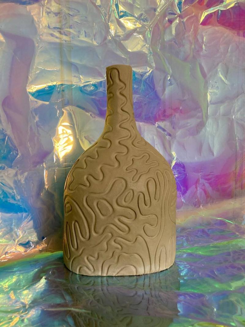 Ceramic vase with a bottle neck shape, with relief drawings on the surface. Photographed on an iridescent background of blues, purples, pinks and greens.