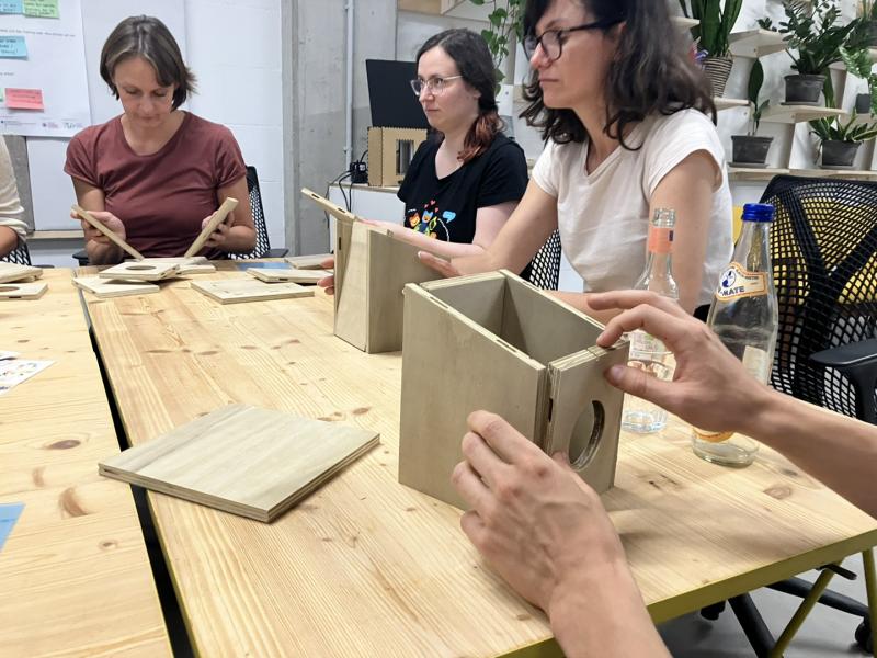 Auf dem Bild sind Teilnehmende eines Workshops zu sehen, die Vogelhäuser zusammenbauen.
