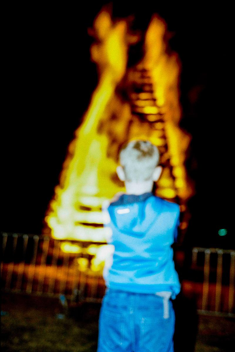 Junge im blauen Trainingsanzug von hinten vor brennendem Maifeuer