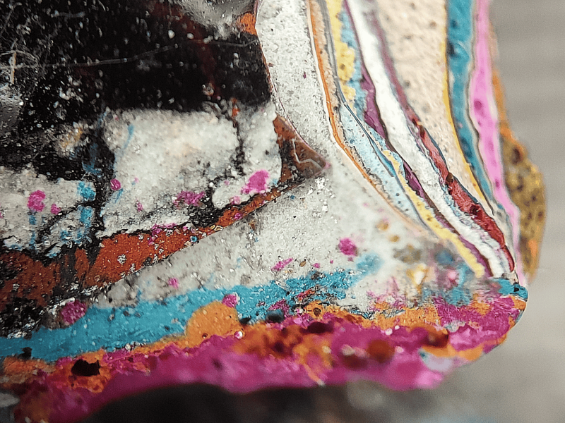 Gezeigt wird ein Ausschnitt eines Graffiti-Fragments, wobei deutlich mehrere Farbschichten, also die Entstehung an der Graffitiwand, zu sehen sind. A section of a graffiti fragment is shown, whereby several layers of paint, i.e. the creation of the graffiti wall, can be clearly seen.
