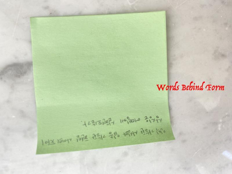 Ein hellgrüner Postit liegt auf einer Steinplatte. Auf dem unteren Teil des post it sind handschriftlich zwei Zeilen auf Koreanisch geschrieben. In roter Schrift steht "Words Behind Form".