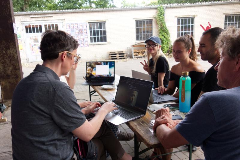Workshopteilnehmende sitzen vor Laptops an einem Holztisch und erstellen KI-Bilder.