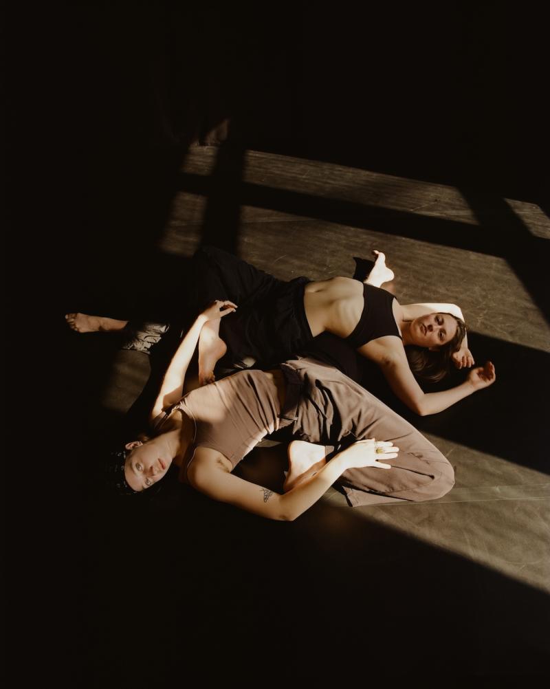 two people lay contorted on floor and look up at camera