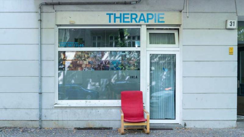 Zu sehen ist ein Schaufenster, in welchem Bilder ausgestellt sind. Die Reflexionen der Bäume legen sich wie ein Filter auf die Scheibe.