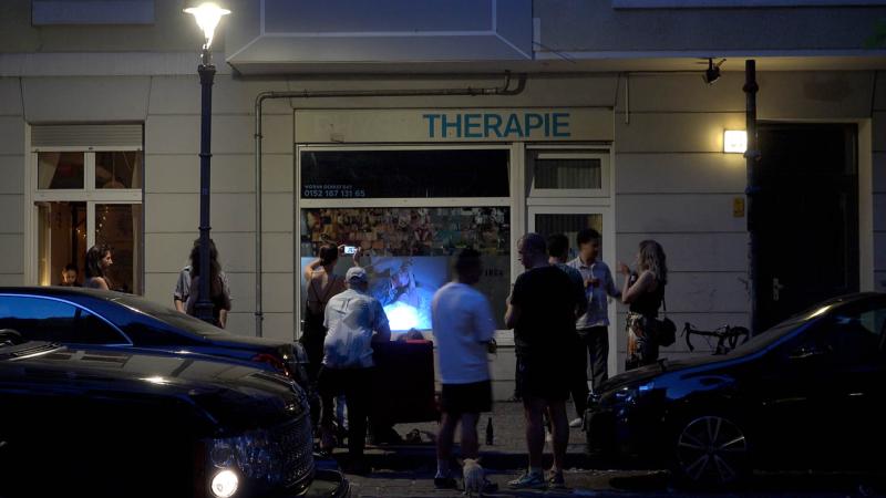 Eine Menschengruppe steht vor dem Schaufenster am Abend und betrachtet die im Fenster ausgestellten Arbeiten.