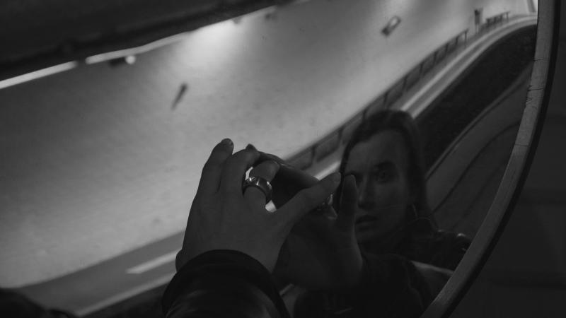 Schwarz-weiß Fotografie von einer Person die an einer U-Bahn Station einen Spiegel berührt.