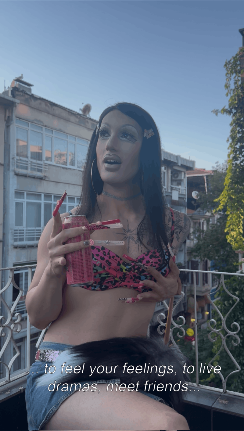 A person with long nails and green eye makeup sits on a balcony wearing a leopard-print bikini top and denim skirt. They hold a pink soda in their right hand and a black and white hair tail on their lap. The sky is clear and the weather sunny. Subtitles read: ... to feel your feelings, to live dramas. meet friends ...