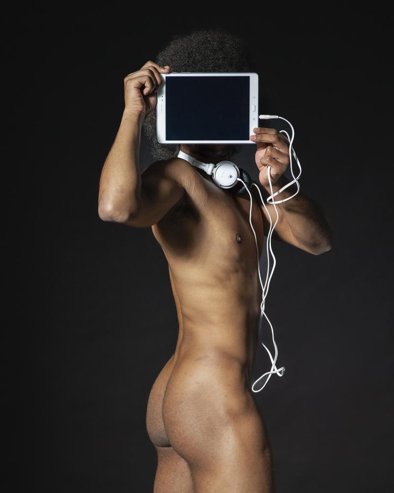 Eine unbekleidete männliche Figur hat ihr Gesicht mit einem elektronischen Gerät namens Tablet verdeckt.