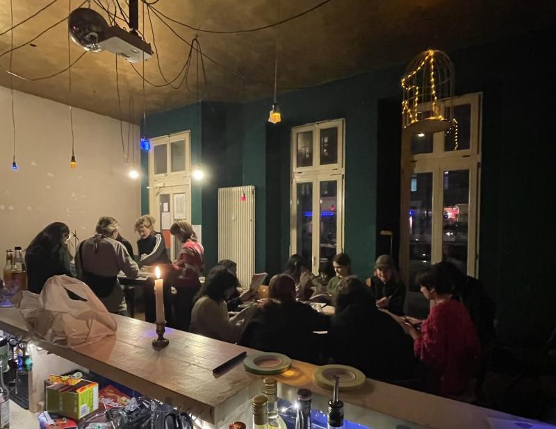 Zu sehen ist eine Gruppe von Menschen, die während einer Veranstaltung des Kollektivs plausch, in der Kollektiv Bar ES an Tischen sitzen und basteln.