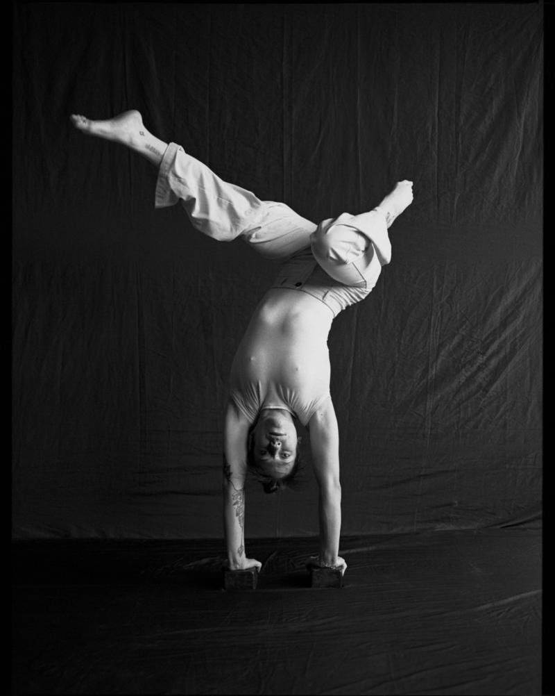 Léo (a person) is doing a handstand with wierd legs. They look at the camera.