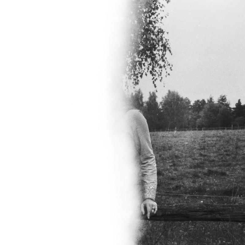 Eine halb belichtete analoge Fotografie einer Person in der Natur, auf einem Zaun sitzend.