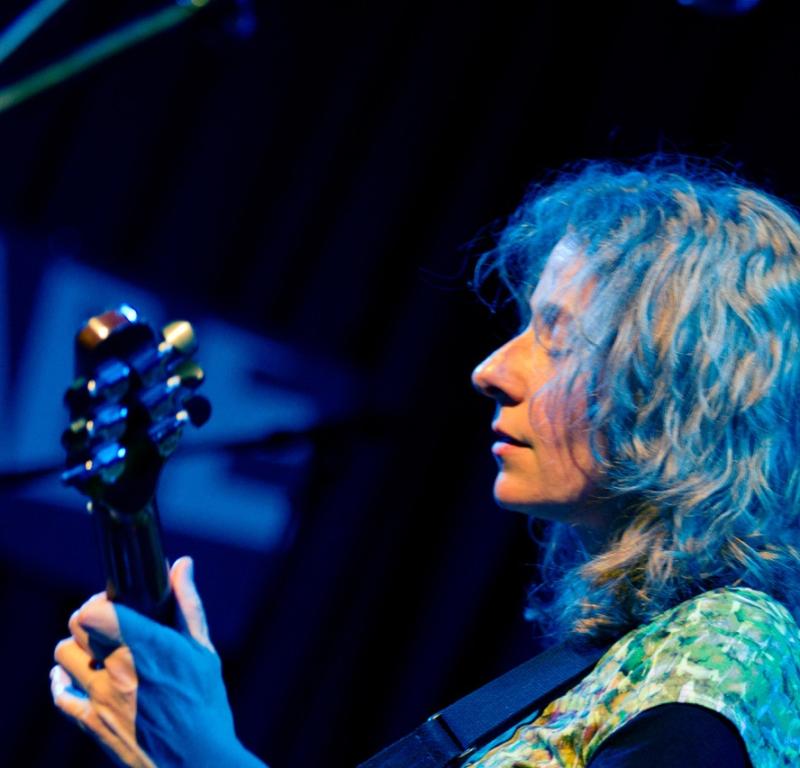 E-Gitarristin mit lockigem Haar spielt auf einer Gitarre auf einer Bühne mit dunklem Hintergrund. Female electric guitarist with curly hair playing a guitar on a stage with a dark background