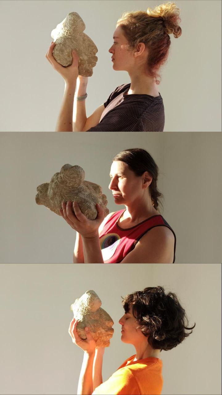3 Performer*innen untereinander mit Steinskulptur in den Händen vorm eigenen Gesicht