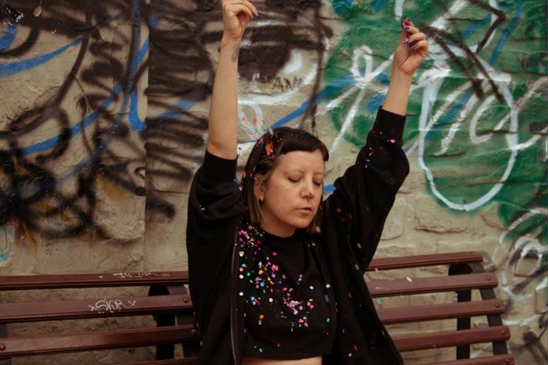 Woman sitting on a street bench is lifting arms and throwing colorful confetti.