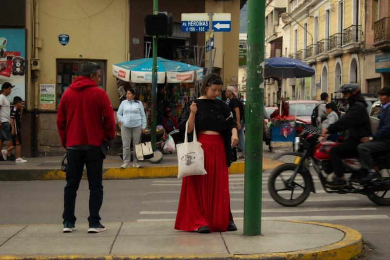 Woman in a long red skirt standing on busy street.