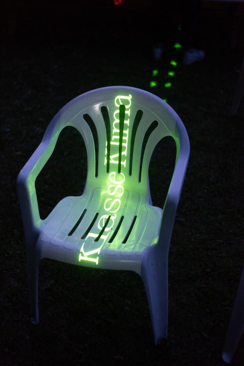 Ein weißer Gartenstuhl, auf den mit grünem Licht Klasse Klima projiziert wird