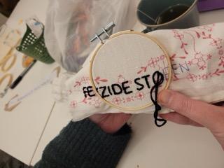Hände an einer Stickerei mit femizide Stoppen darauf