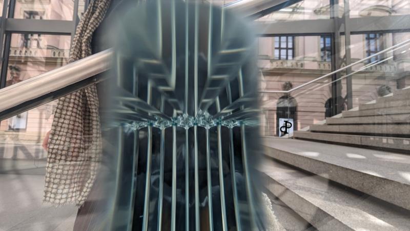 Durch eine Glasscheibe fotografierte Spiegelungen und Lichtbrechungen überlagern eine Treppe und Gebäudefassade und erzeugen eine abstrakte, räumliche Struktur.
