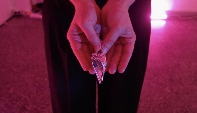 Close-up of hand holding in the palms between thumbs a piece of foil folded into a shape resembling a bud.