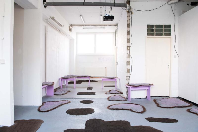A exhibition room with an installation work. Pink and brown textile works lying on the floor and wooden benches.