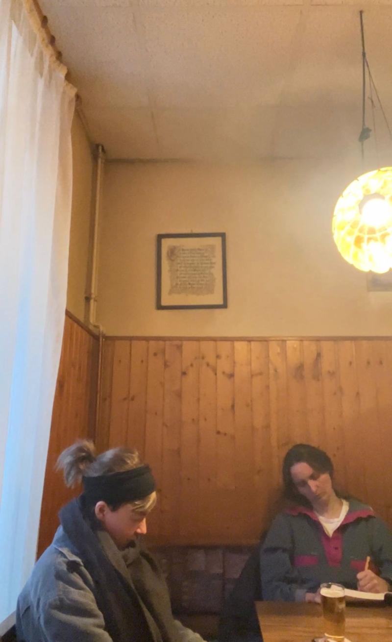 Constanze Klar und Hannah Sehl sitzen an einem Ecktisch in einer Kneipe und schreiben Briefe