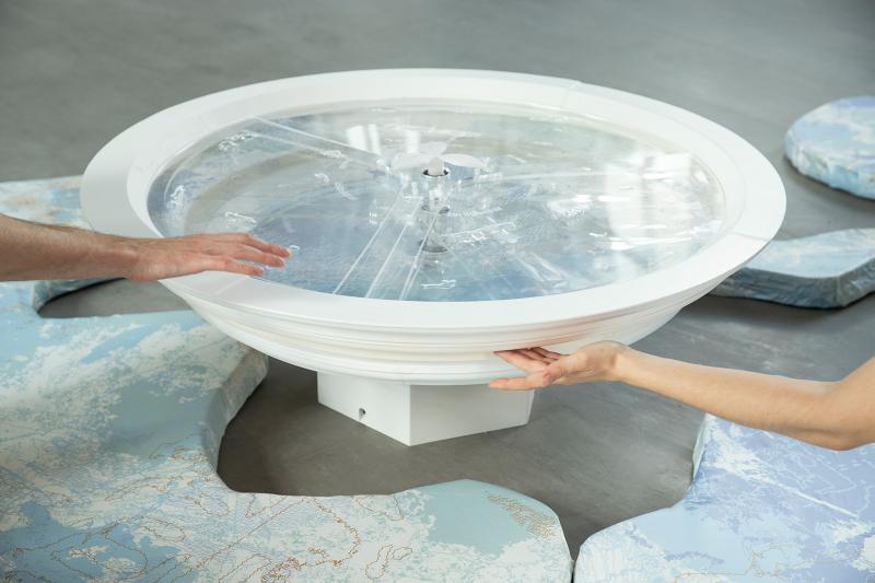 Das Bild zeigt einen Ausschnitt der Installation "Flowing Gesture". Zu sehen sind zwei Hände, die ein drehbares Brunnenbecken bewegen.