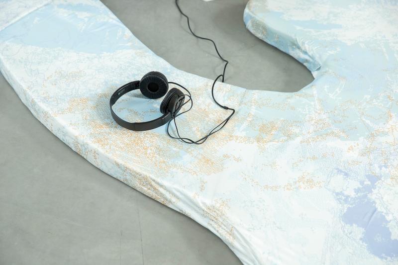 Close up auf die Sitzfläche der Installation "Flowing Gesture". Zu sehen ist ein texturiertes Kissen mit organischer Form auf dem ein Kopfhörer liegt.